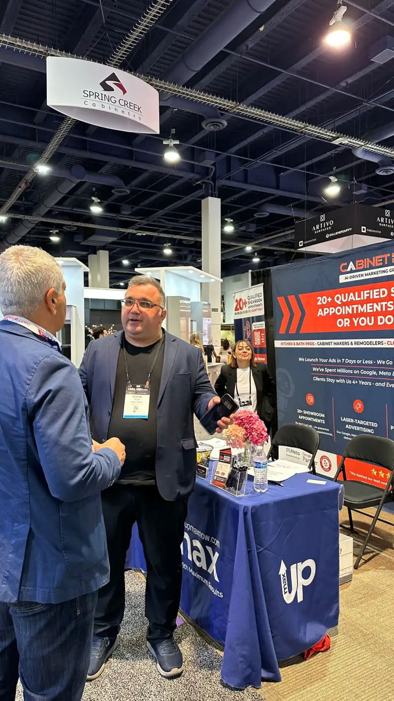 CabinetBoost founder Sezgin Arslan in conversation with a KBIS 2025 attendee at the booth table, Las Vegas Convention Center — UPMAX-branded table visible